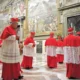 Cardeais da Igreja Católica caminham pela Capela Sistina durante cerimônia do conclave, vestindo trajes vermelhos tradicionais, sob afrescos renascentistas e vigilância da Guarda Suíça.