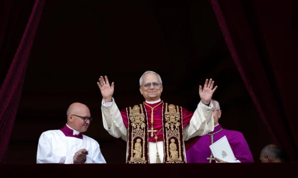 Novo Papa Leão XIV acena ao público da varanda da Basílica de São Pedro, acompanhado por membros do clero, durante sua primeira aparição oficial após a eleição