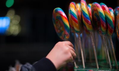 Mão de criança segurando um pirulito grande e colorido entre vários outros, todos dispostos em pé em uma caixa de exposição.